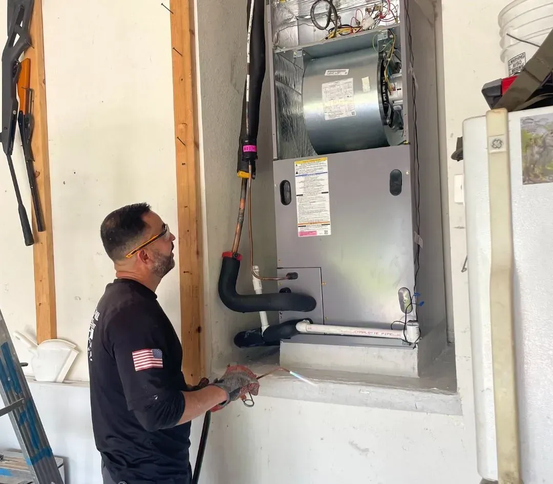Technician inspecting a gray HVAC furnace unit installed in a wall cavity.