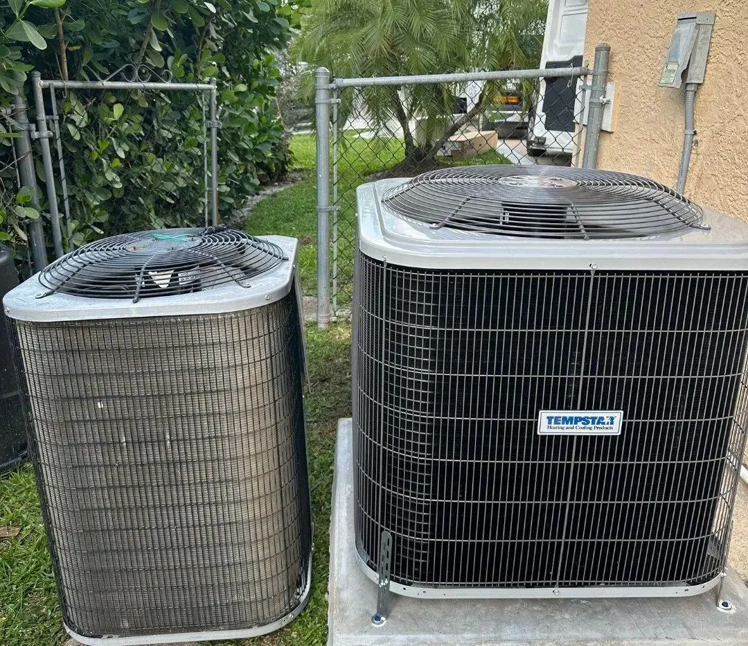 Two outdoor air conditioning units beside a house, one round and one square.