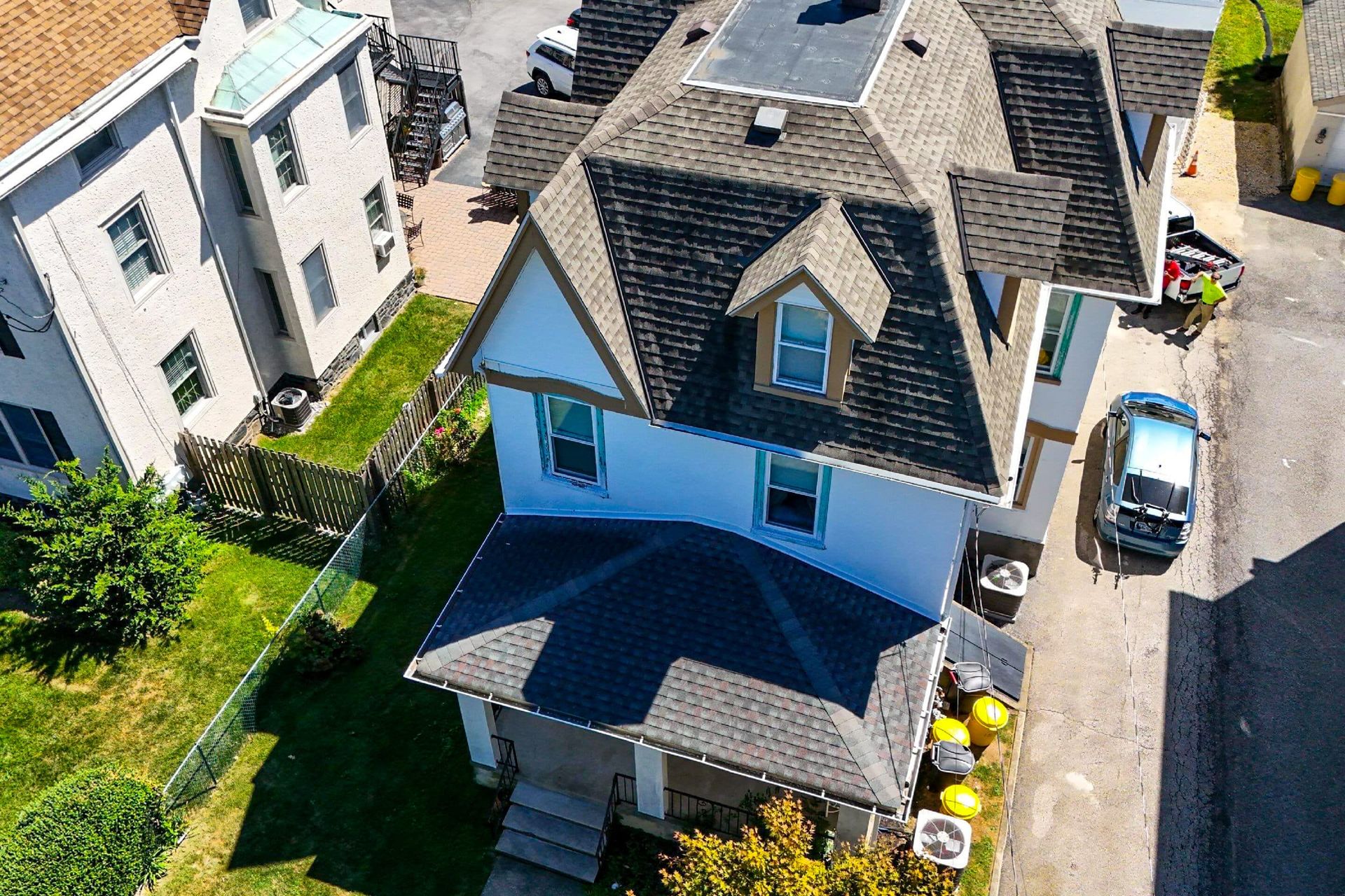 An aerial view of a two-story white house with a dark shingled roof, a front porch, and a car parked in the driveway.