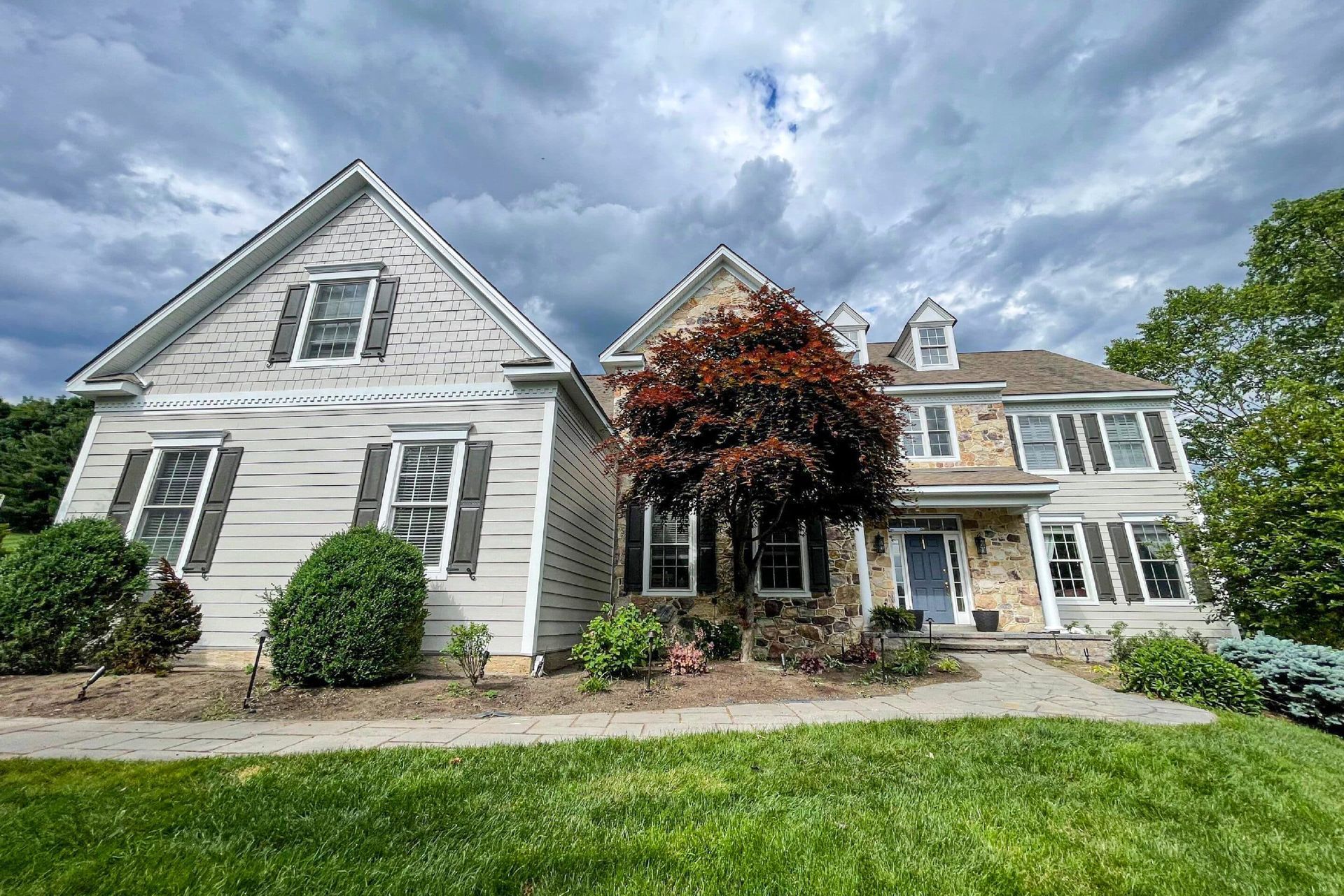 A multi-story home with a stone and light-colored siding exterior, framed by green landscaping under a cloudy sky.