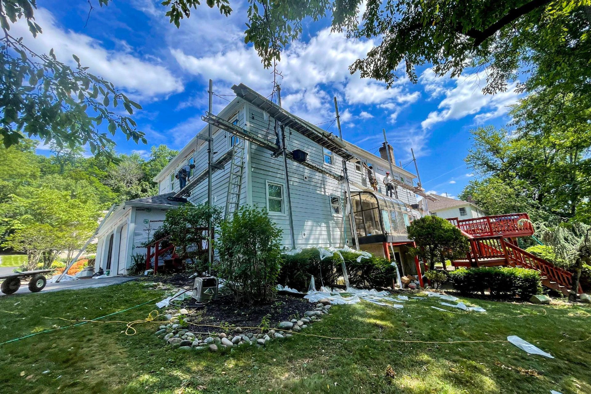 A two-story white house undergoing exterior renovation with scaffolding and ladders against the siding.