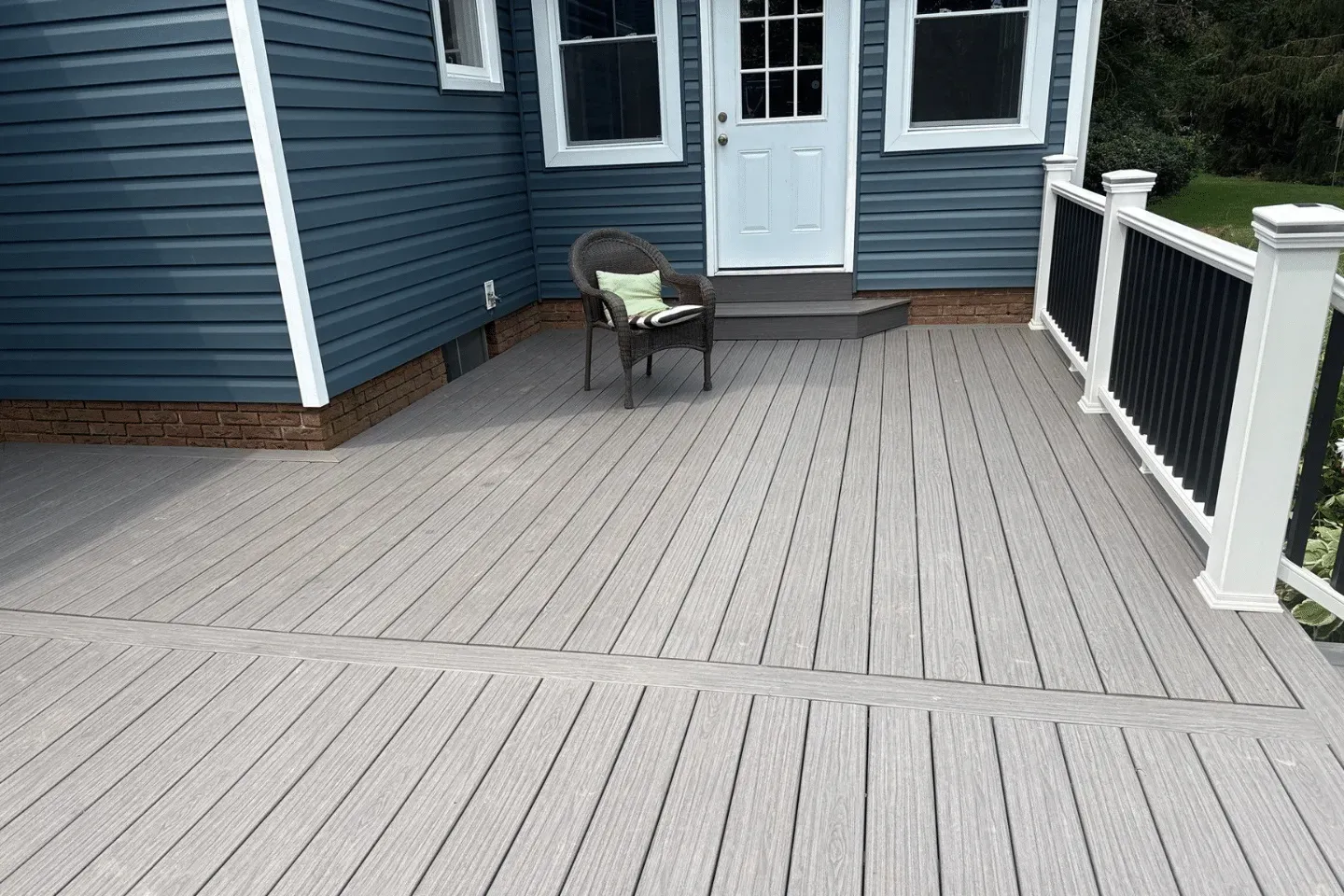 A grey composite deck with a single outdoor chair, white railing, and blue siding on a home exterior.