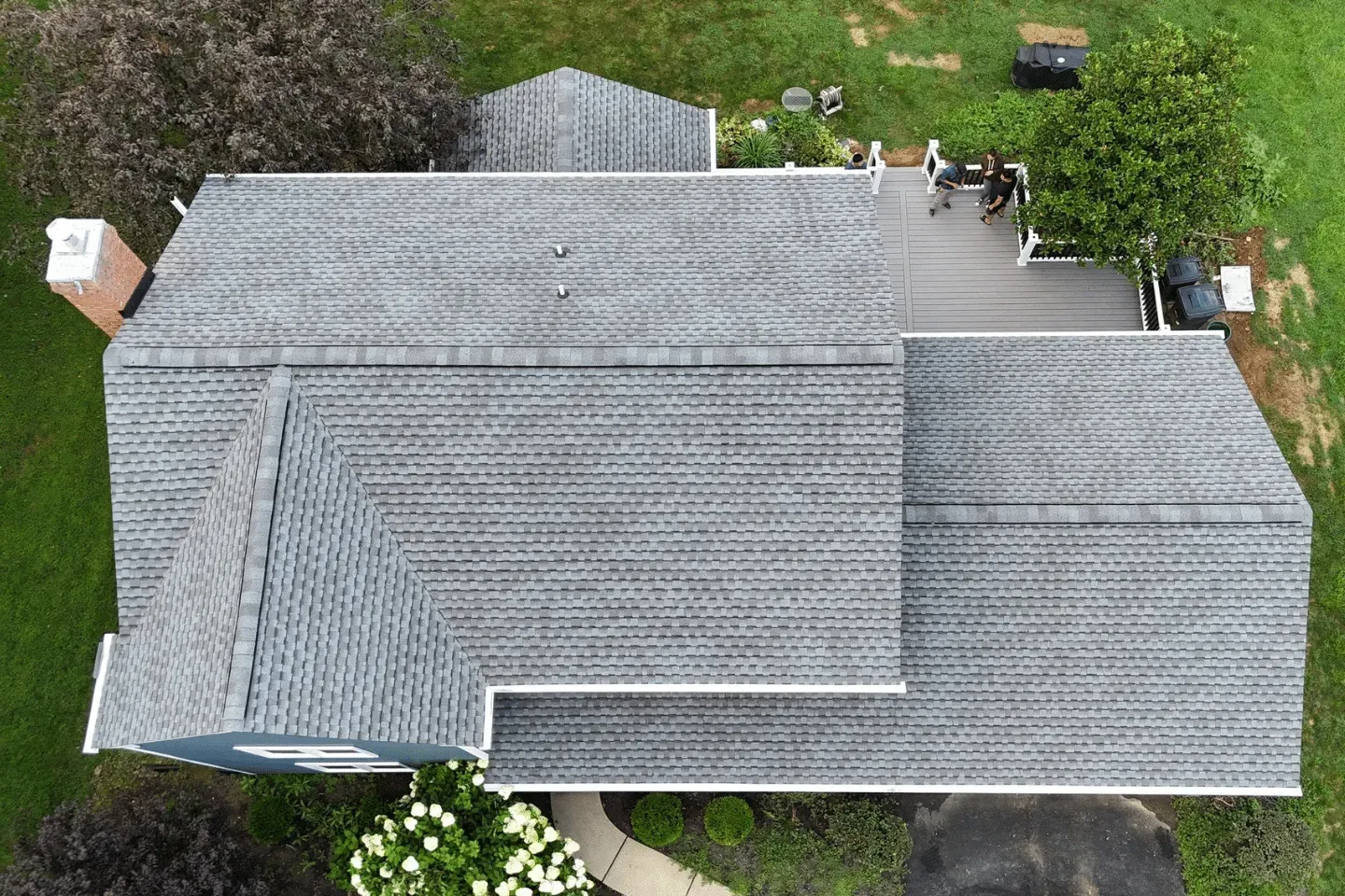 An aerial view of a gray shingled residential roof, showing the roof layout, a deck, and surrounding green lawn.