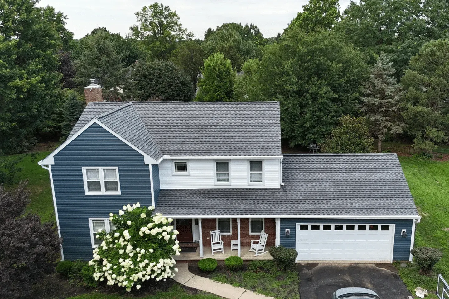 An aerial view of a two-story suburban house with blue siding, a white middle section, and an attached two-car garage.