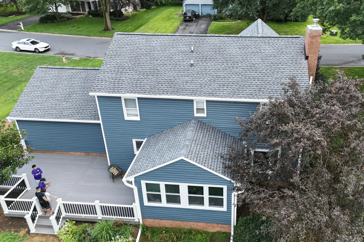 An aerial view of a blue two-story house with a grey roof, a back deck, and three people standing on the deck.
