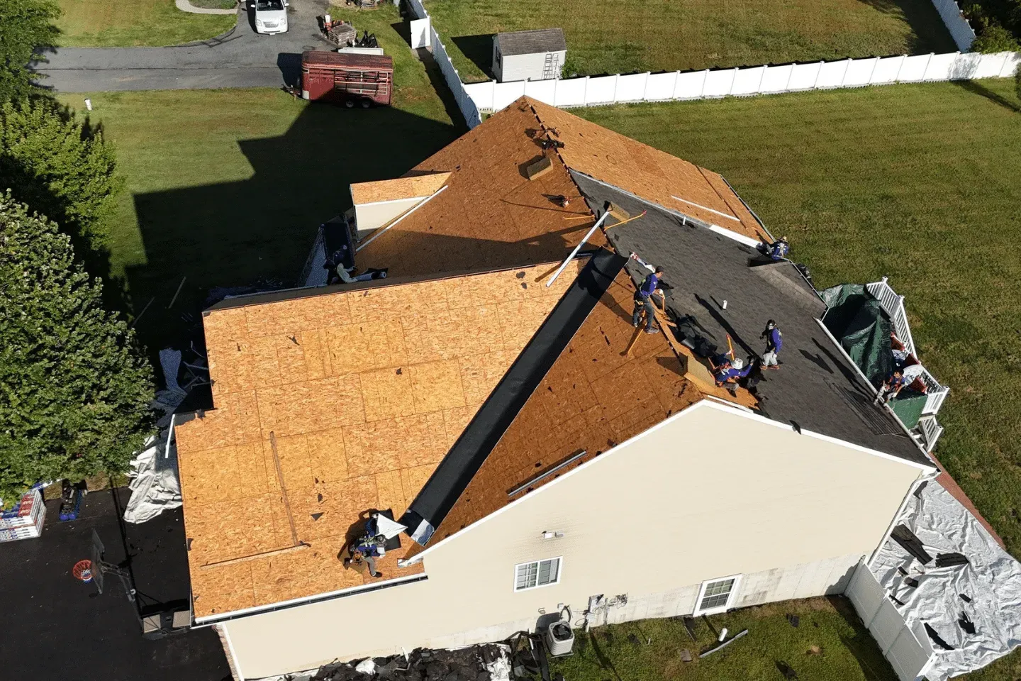 An aerial view shows workers installing new plywood sheathing on a house roof during a residential construction project.
