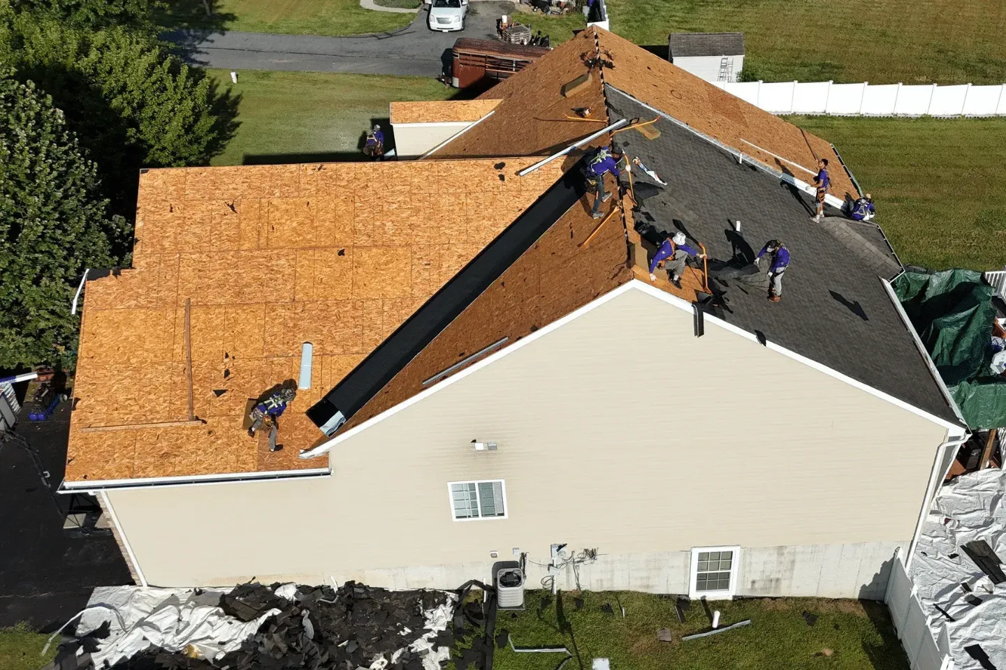 An aerial view of roofers installing shingles on a residential home with partial wood decking exposed.