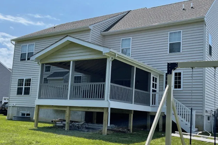 A two-story light-colored house featuring a large, covered screened-in porch with a wooden deck and white stairs.