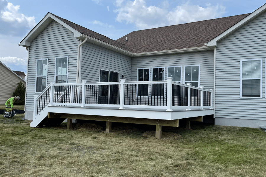 A newly constructed white deck with metal railings attached to the back of a gray-sided suburban home.