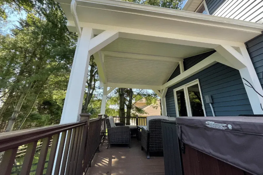 A covered deck featuring a white wooden structure, dark blue siding, outdoor seating, and a hot tub.
