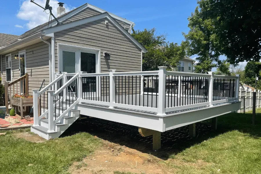 A gray house with a new, raised wooden deck featuring white railings, black balusters, and stairs leading to the yard.