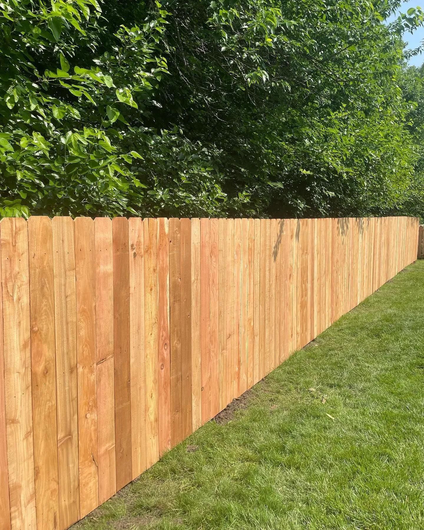 Wooden fence in a yard with green grass and trees in the background.