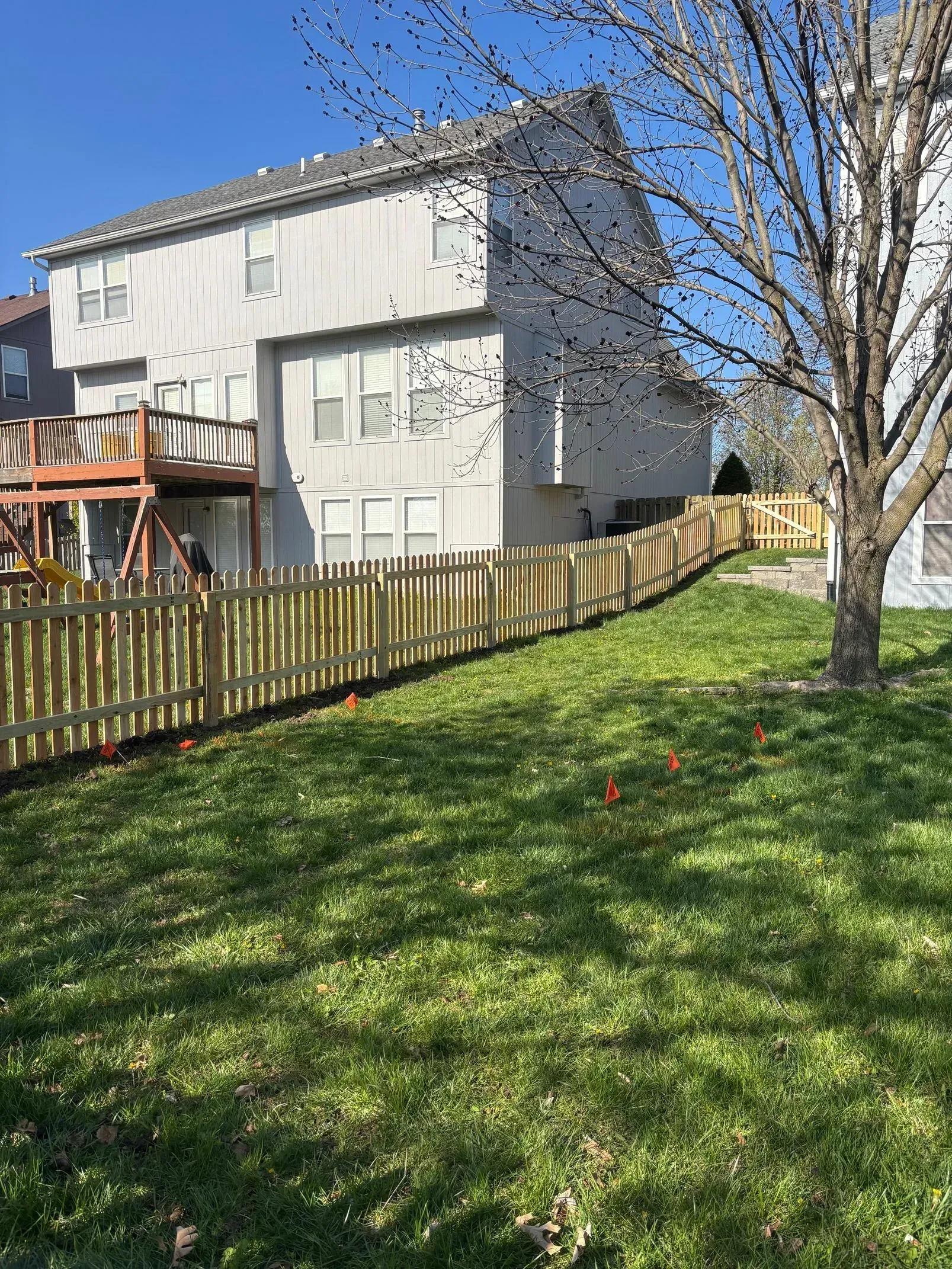 Wooden fence along a grassy backyard, beside a two-story house, sunny day.