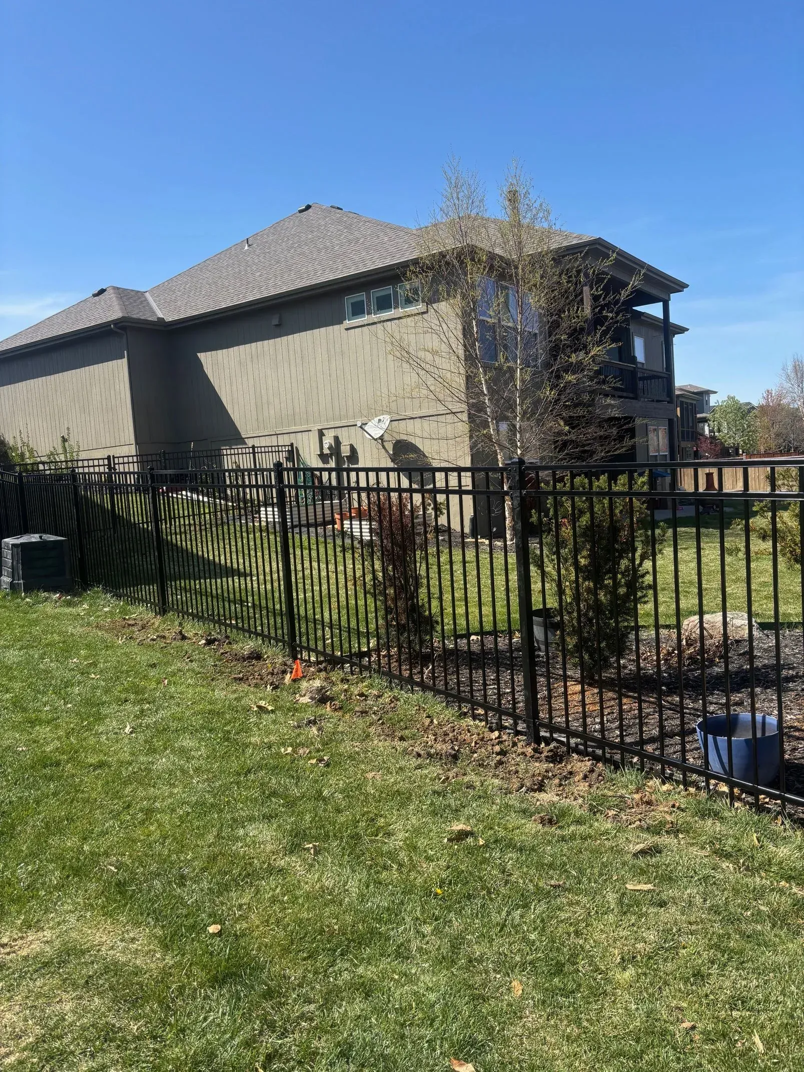 Black metal fence in front of a house with a gray roof and green yard.