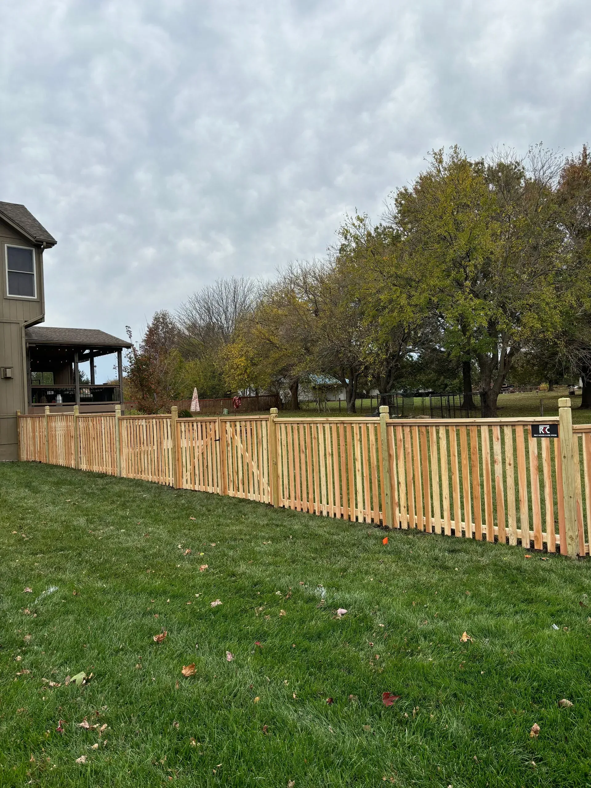Wooden fence alongside a house and grassy yard under a cloudy sky.