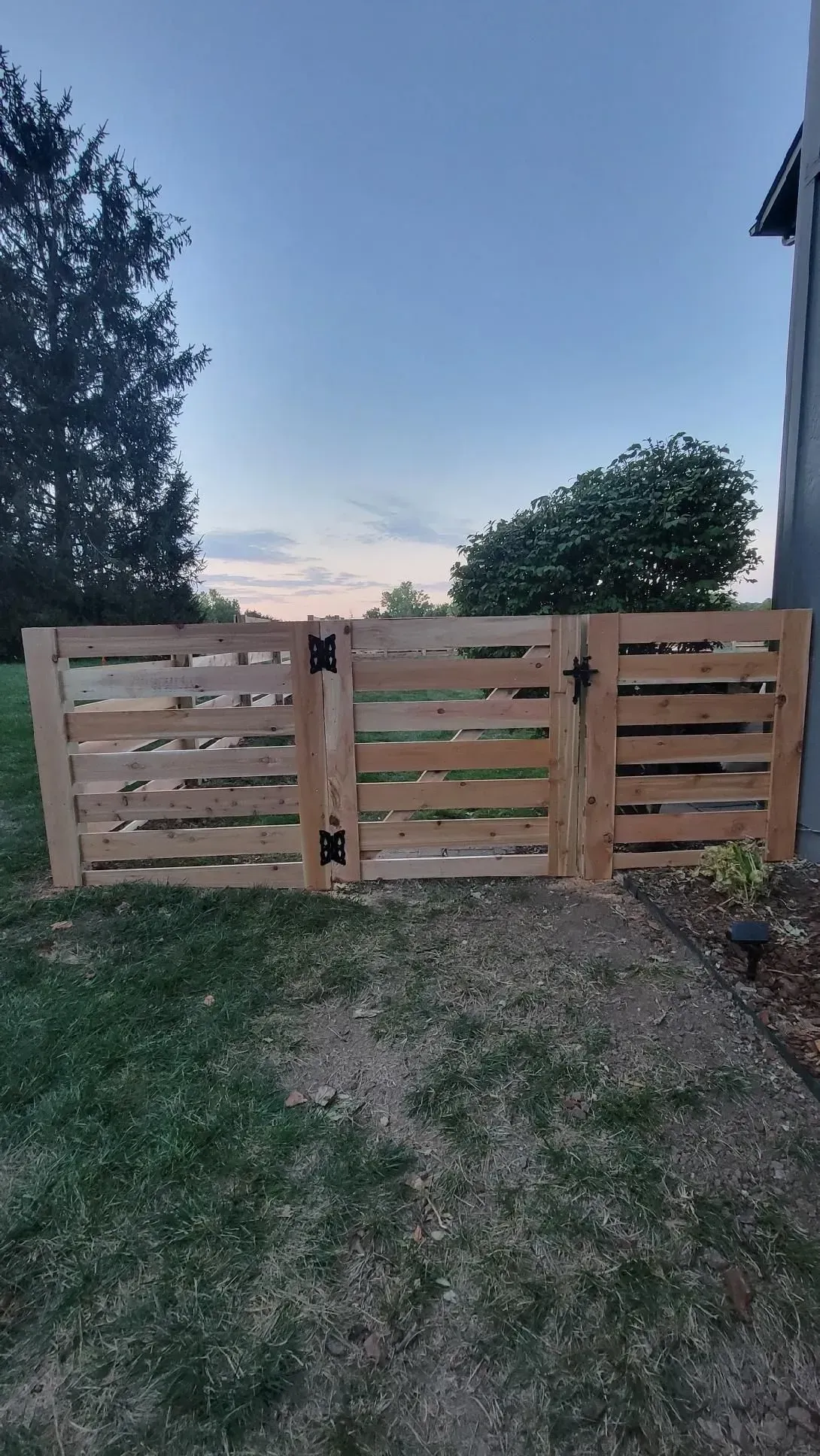 Wooden fence made from pallets, with hinges and a latch. Grass and a cloudy sky in the background.