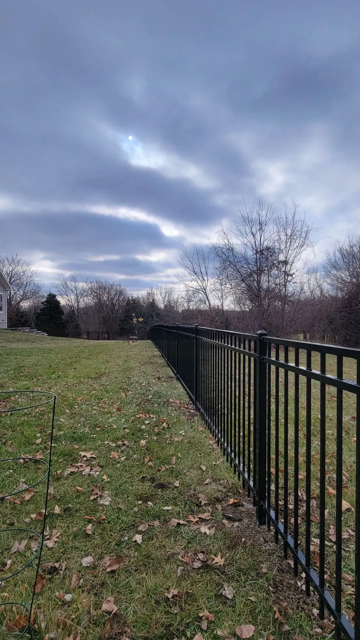 Black metal fence along a grassy yard under a cloudy sky.
