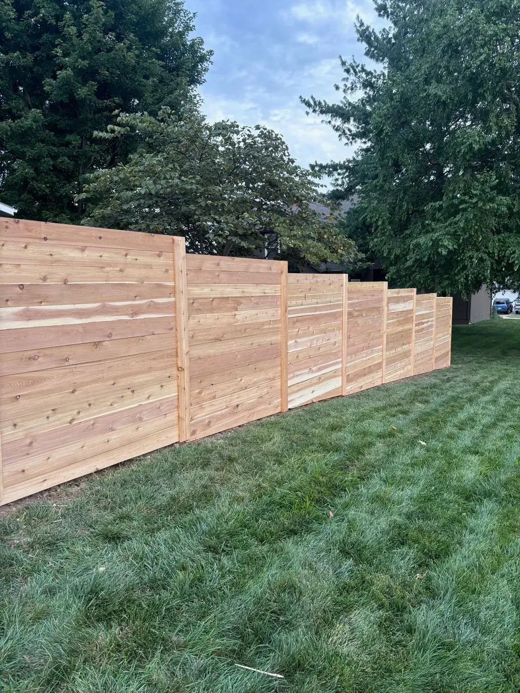 A newly built wooden fence in a grassy yard, with trees in the background.