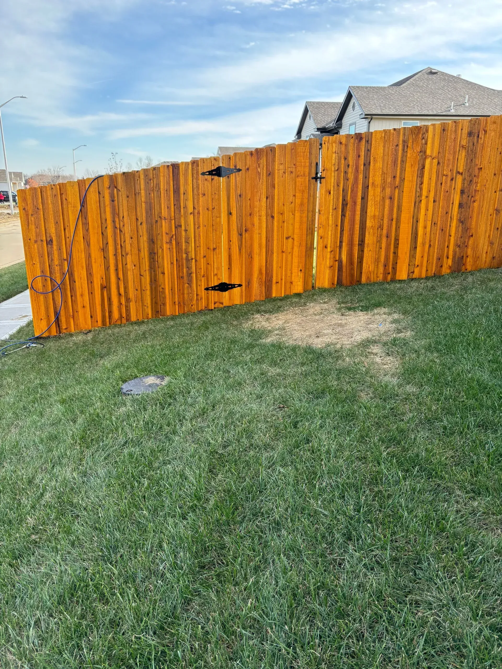 Wooden fence stained brown, with black hinges, on a grassy hill.