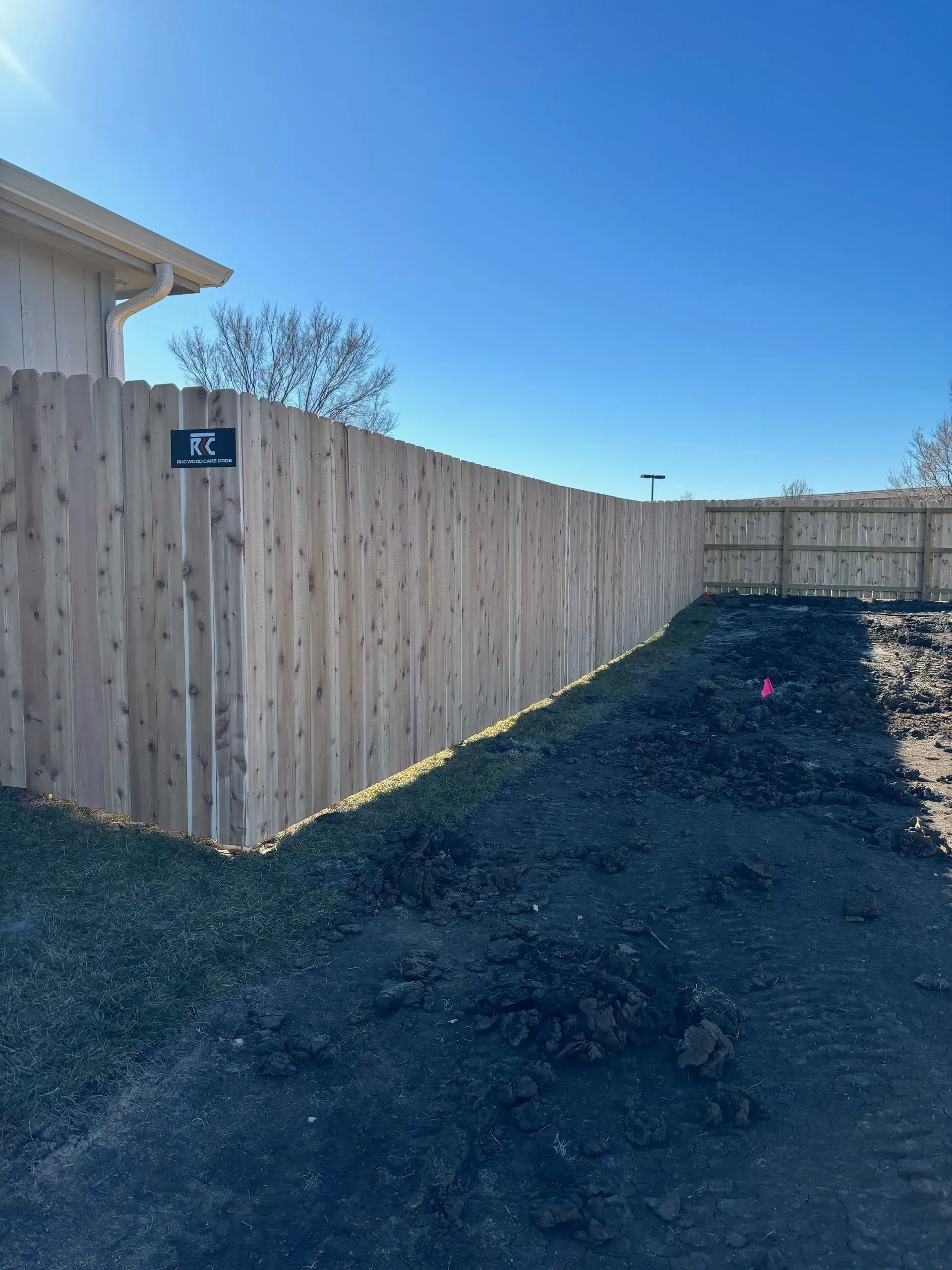 Wooden fence along a yard with dark soil and bright blue sky.