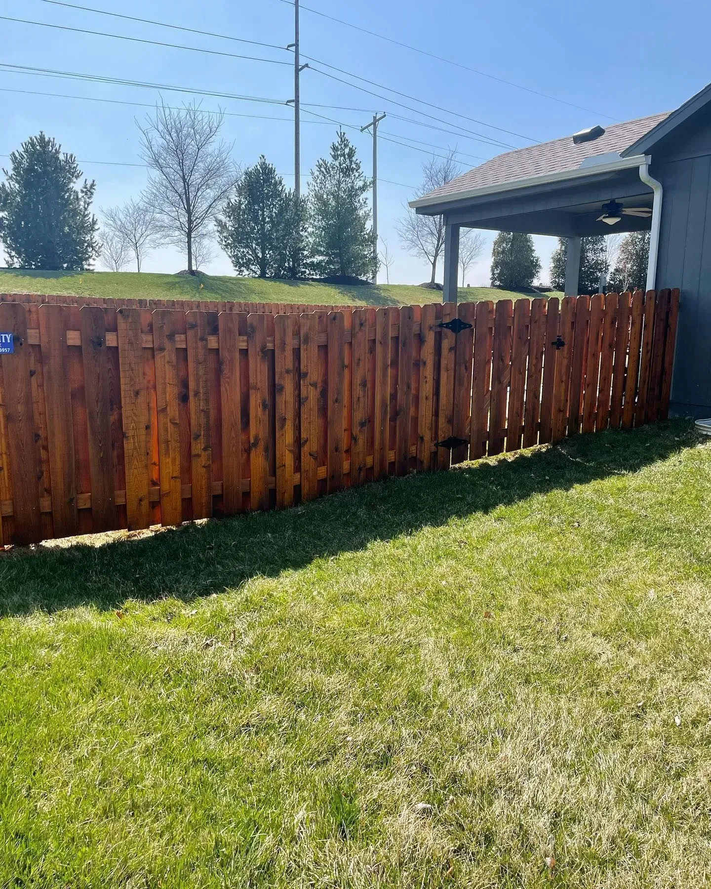 Wooden fence stained brown, surrounding a grassy yard next to a house.