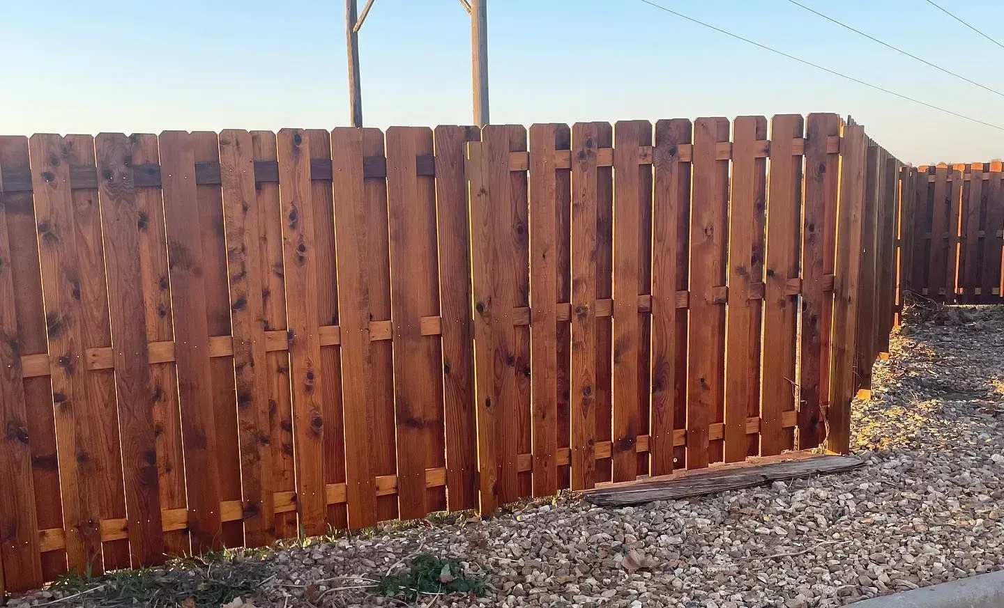 Brown wooden fence along a gravel area with a clear sky in the background.