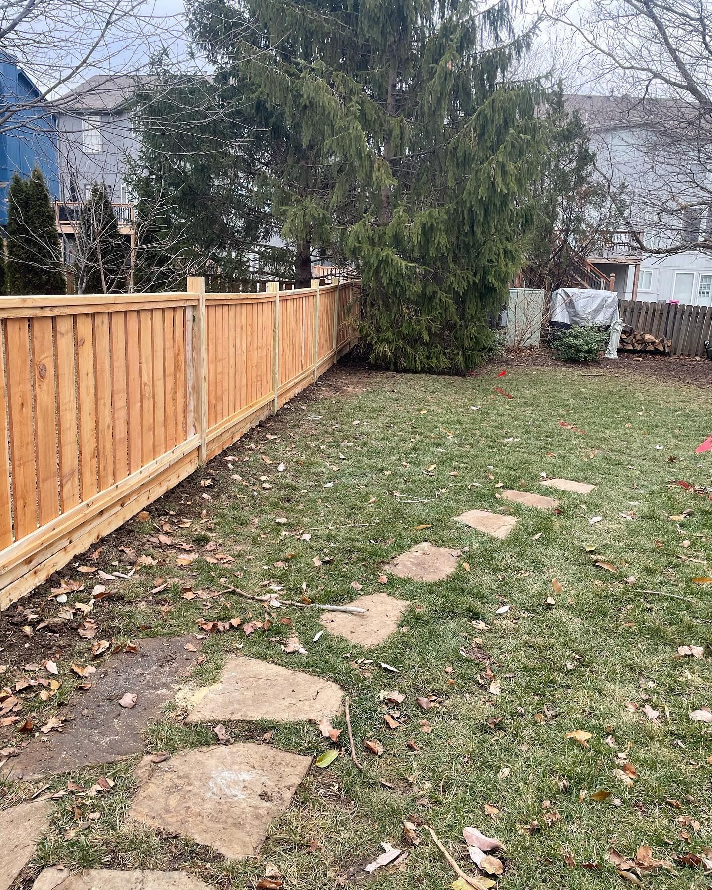 Wooden fence borders a grassy backyard with stone pathway and tree.