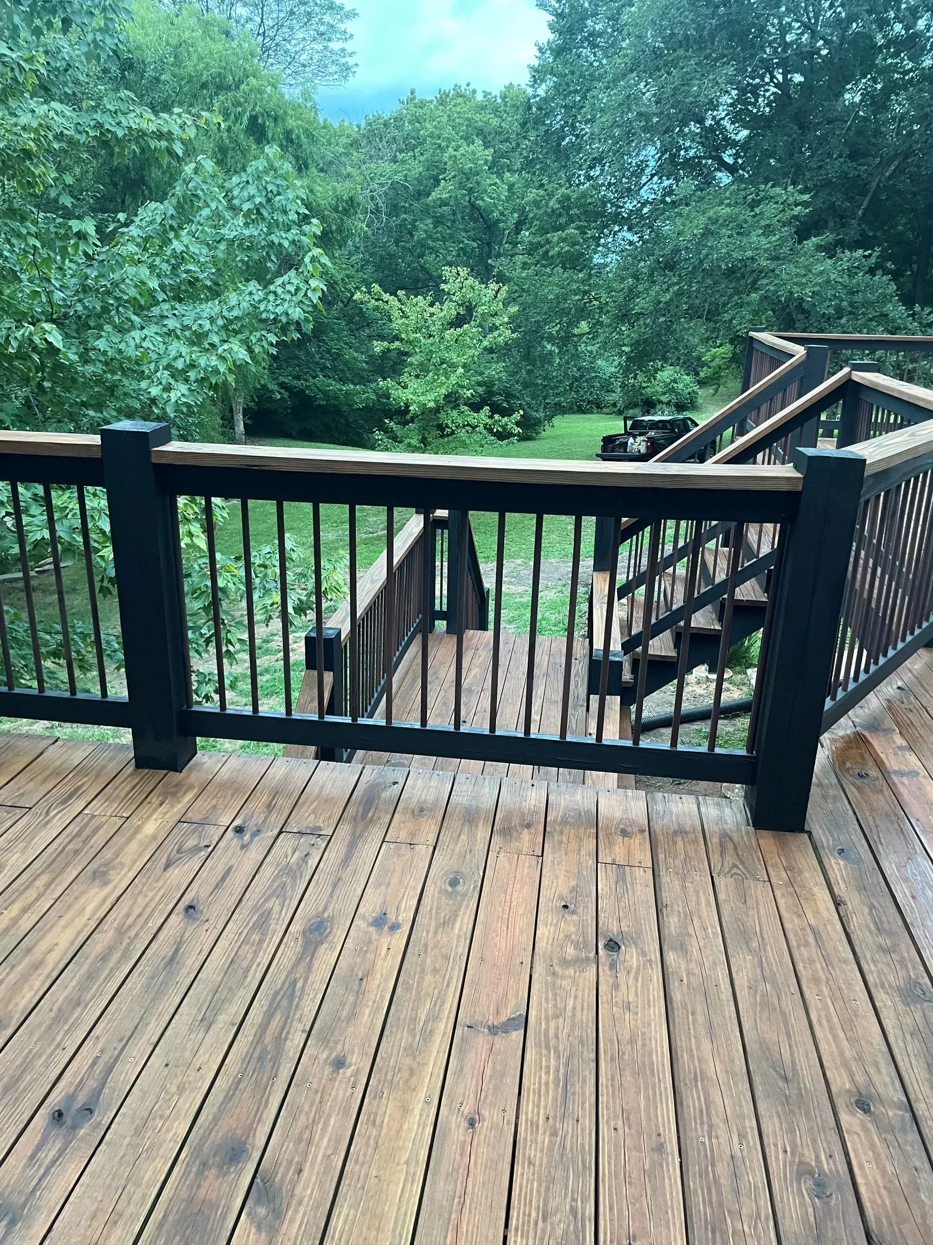 Wooden deck with railings, steps leading down, surrounded by trees.