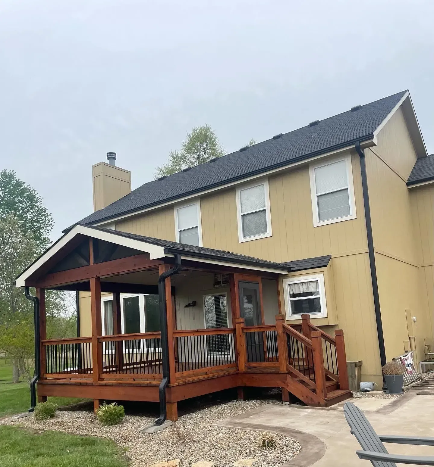 Brown wooden deck and porch attached to a tan two-story house with dark roof.