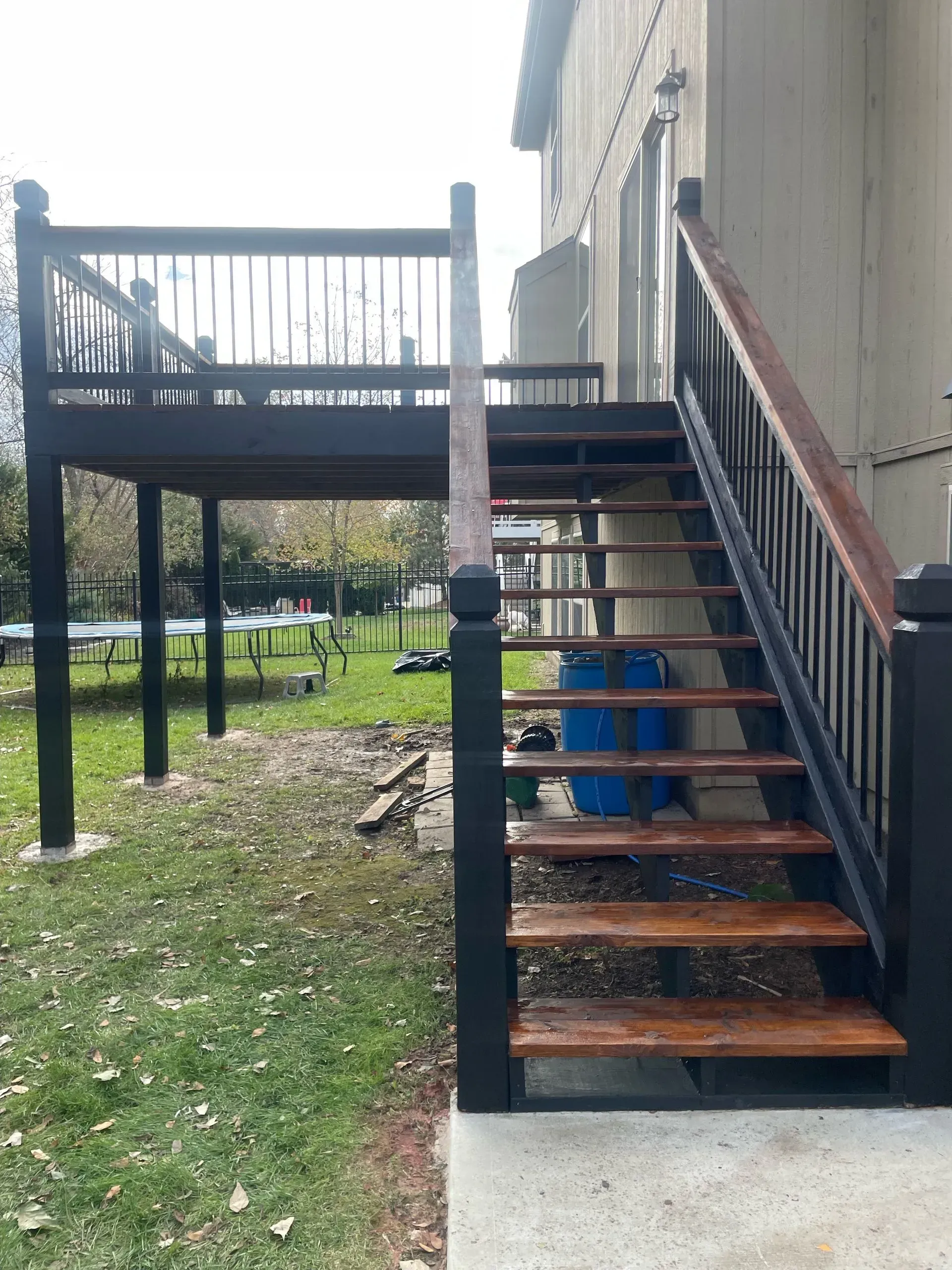 Wooden deck with stairs leading down to a concrete patio. The deck and stairs are dark brown and black.
