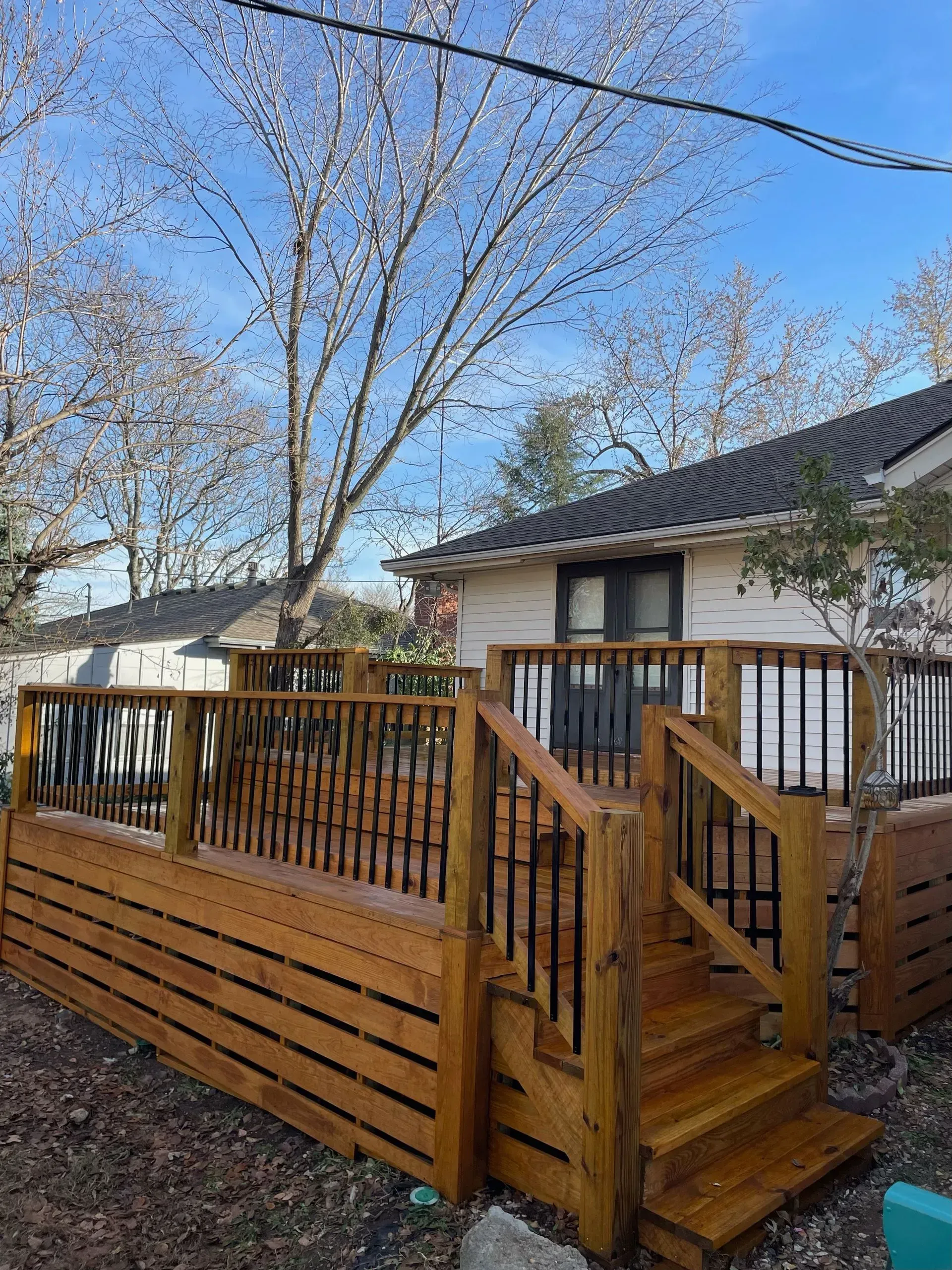 Wooden deck with stairs, black railing, attached to a white house under a blue sky.