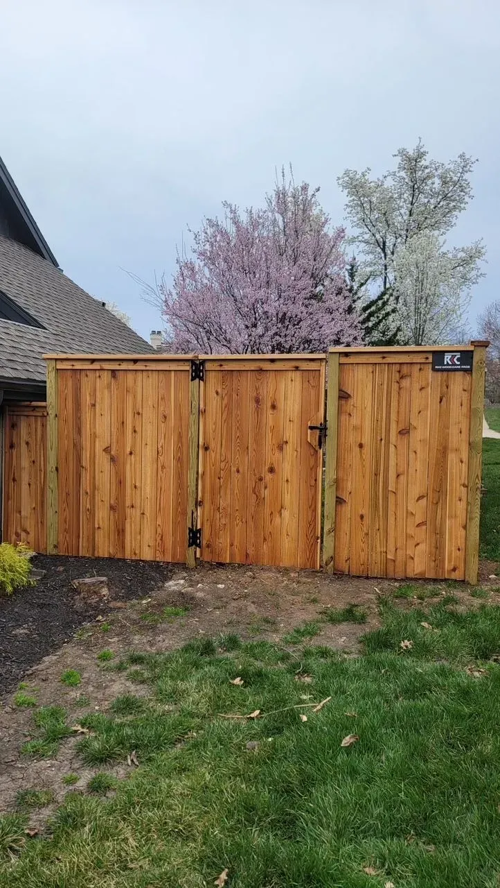 Wooden fence with a gate, in front of a house, spring blossoms in background.