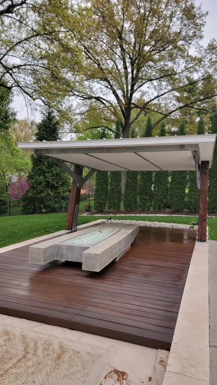 A covered structure with a long stone bench in a park setting. Brown, white, and green tones.
