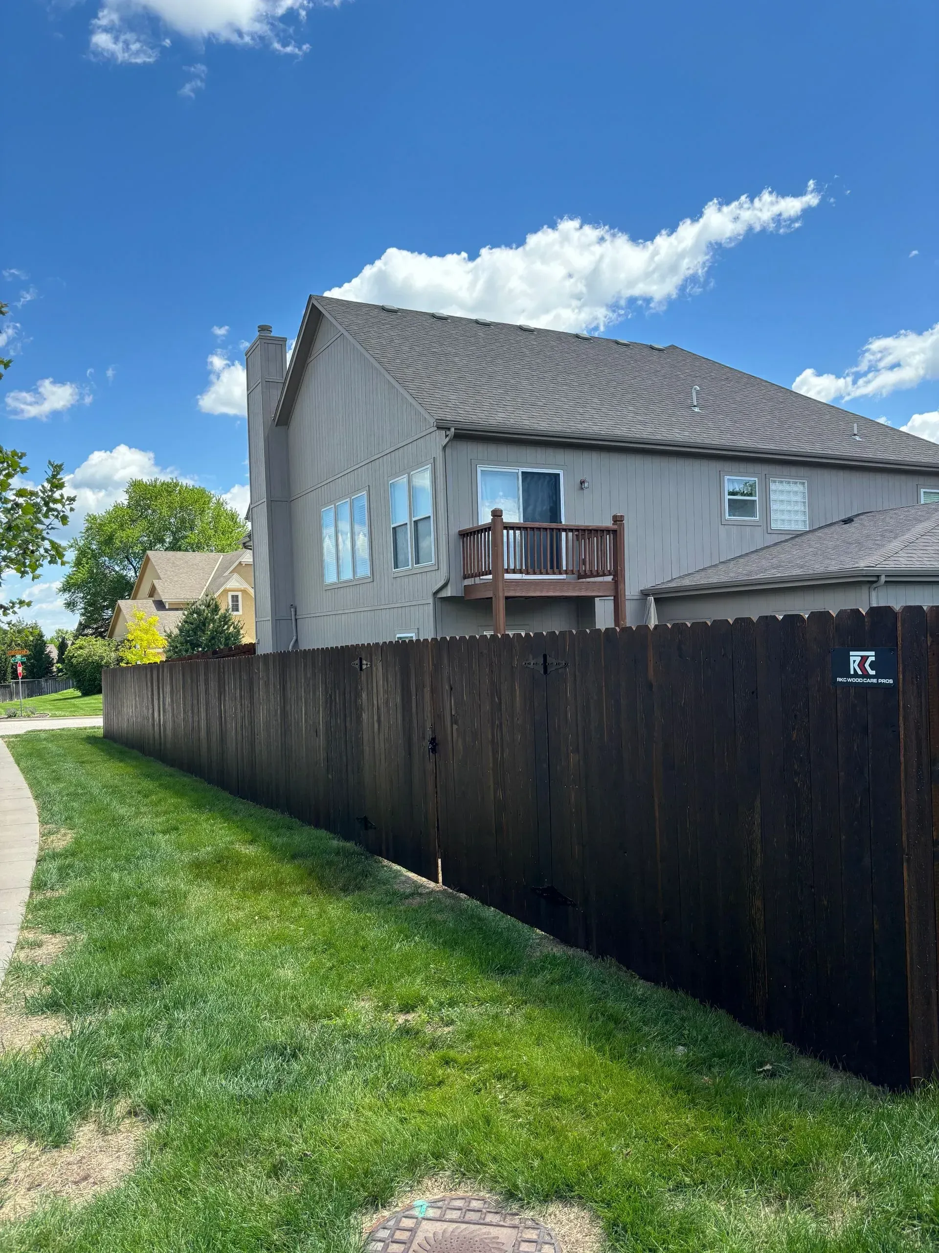 A two-story house with a wooden fence and a small deck under a blue sky.