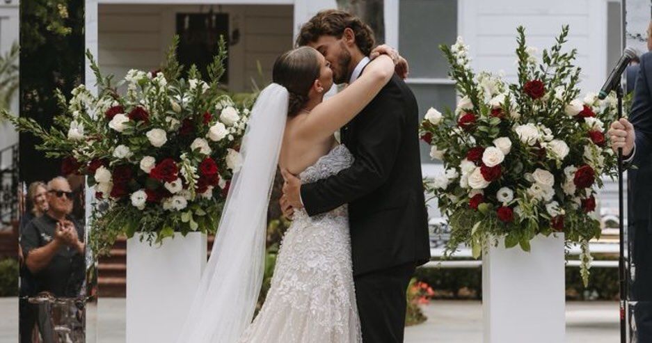 Couple kissing at a wedding ceremony, surrounded by floral arrangements and guests.