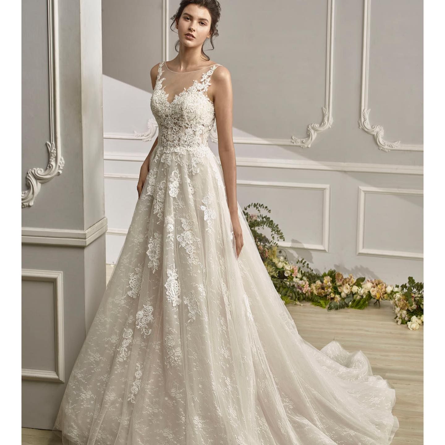 Woman in a white wedding gown, standing in a room with floral decorations.