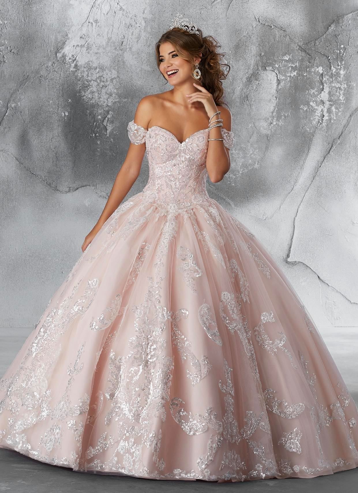 Woman in a pink off-the-shoulder ballgown smiles, posing against a textured backdrop.