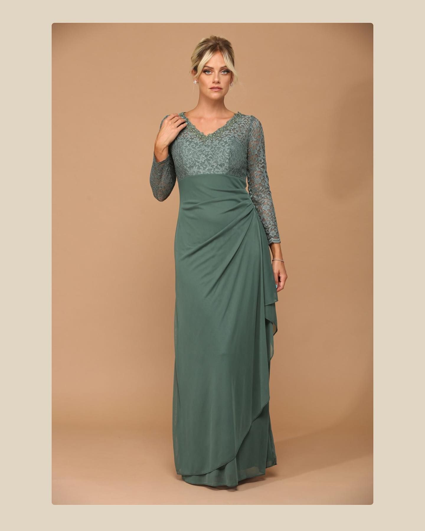 Woman in green formal dress with lace bodice, posing against beige backdrop.