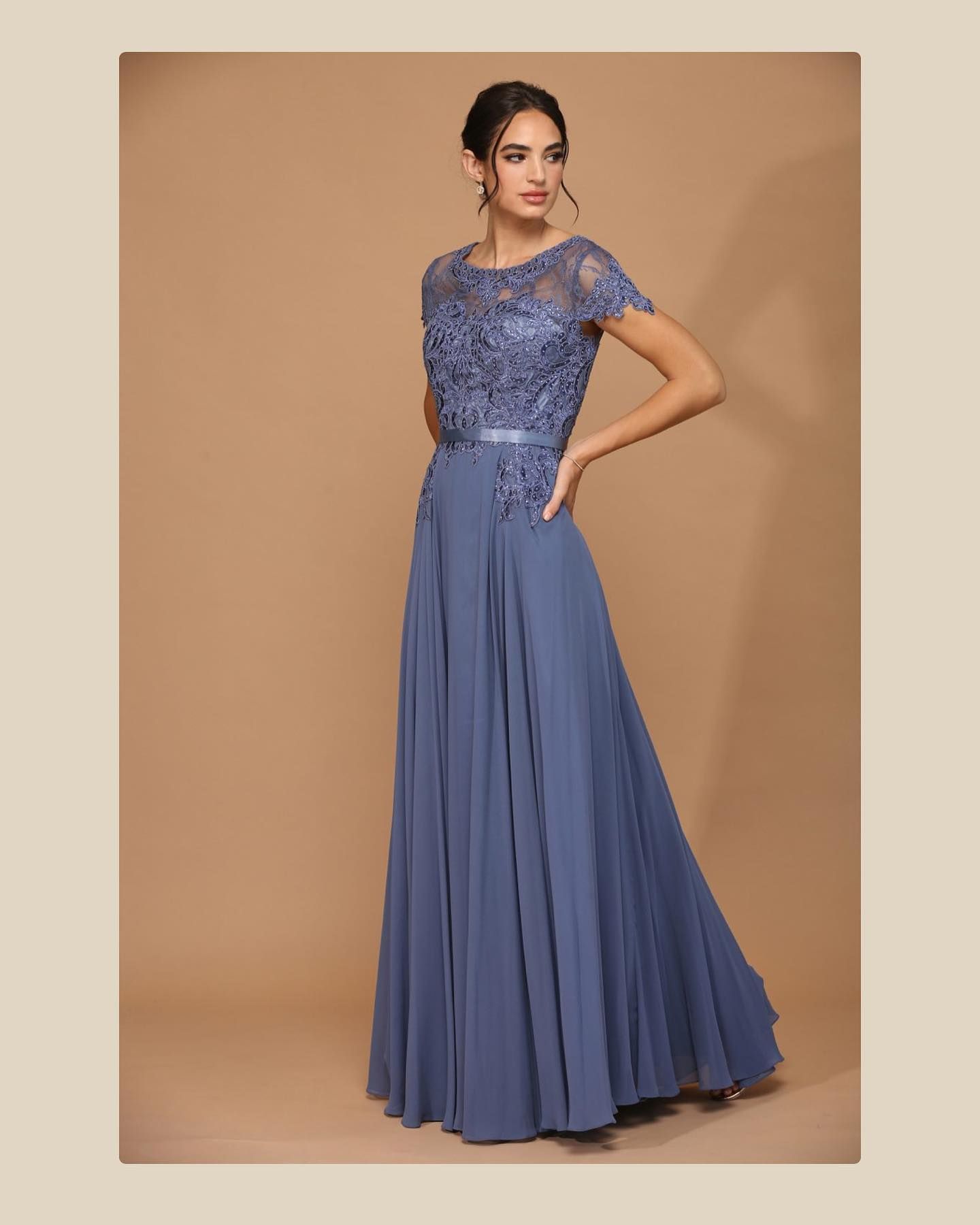 Woman in a blue gown with lace bodice and flowing skirt, posing indoors.