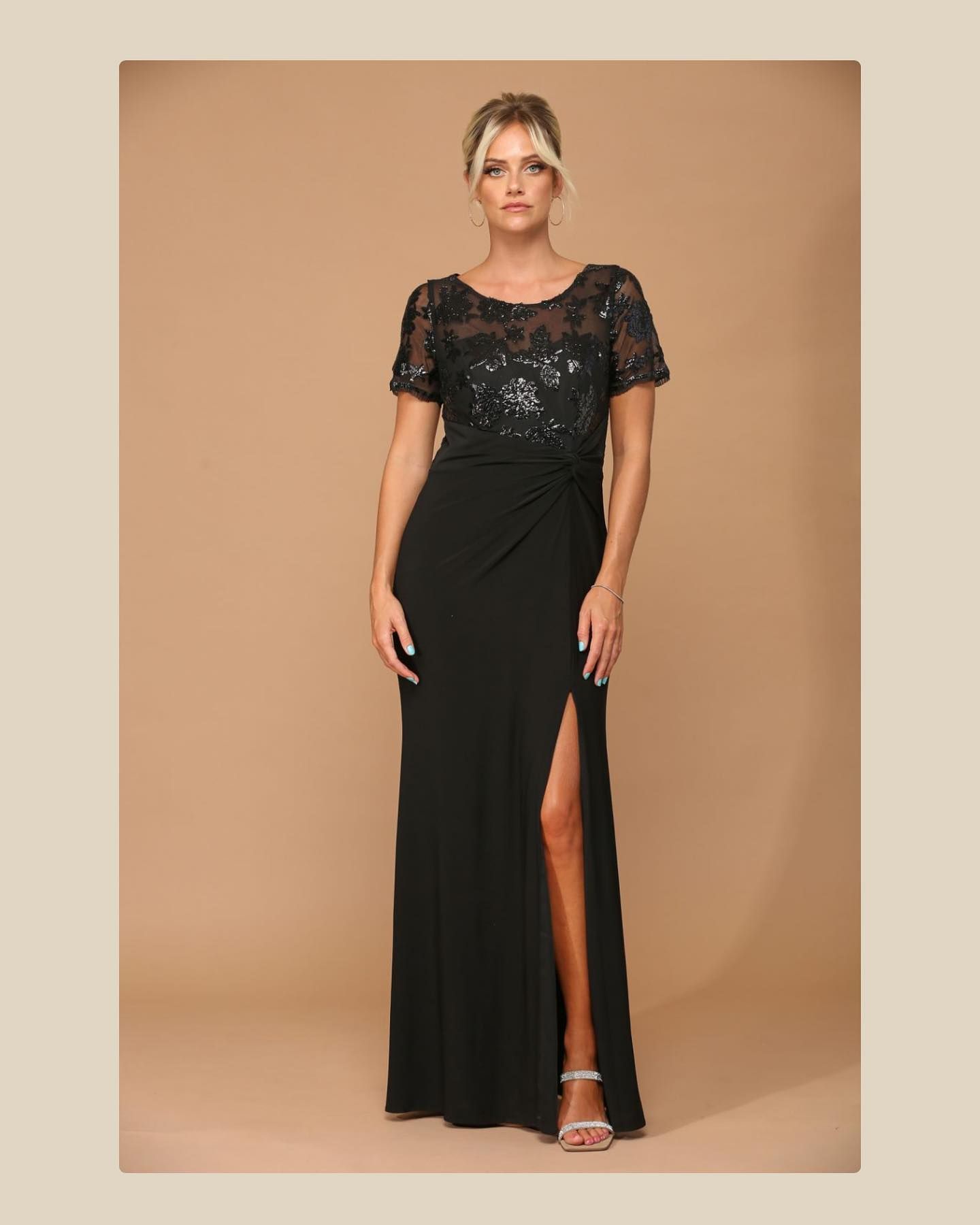 Woman in a black evening gown with a sequined bodice and high slit, standing against a beige backdrop.