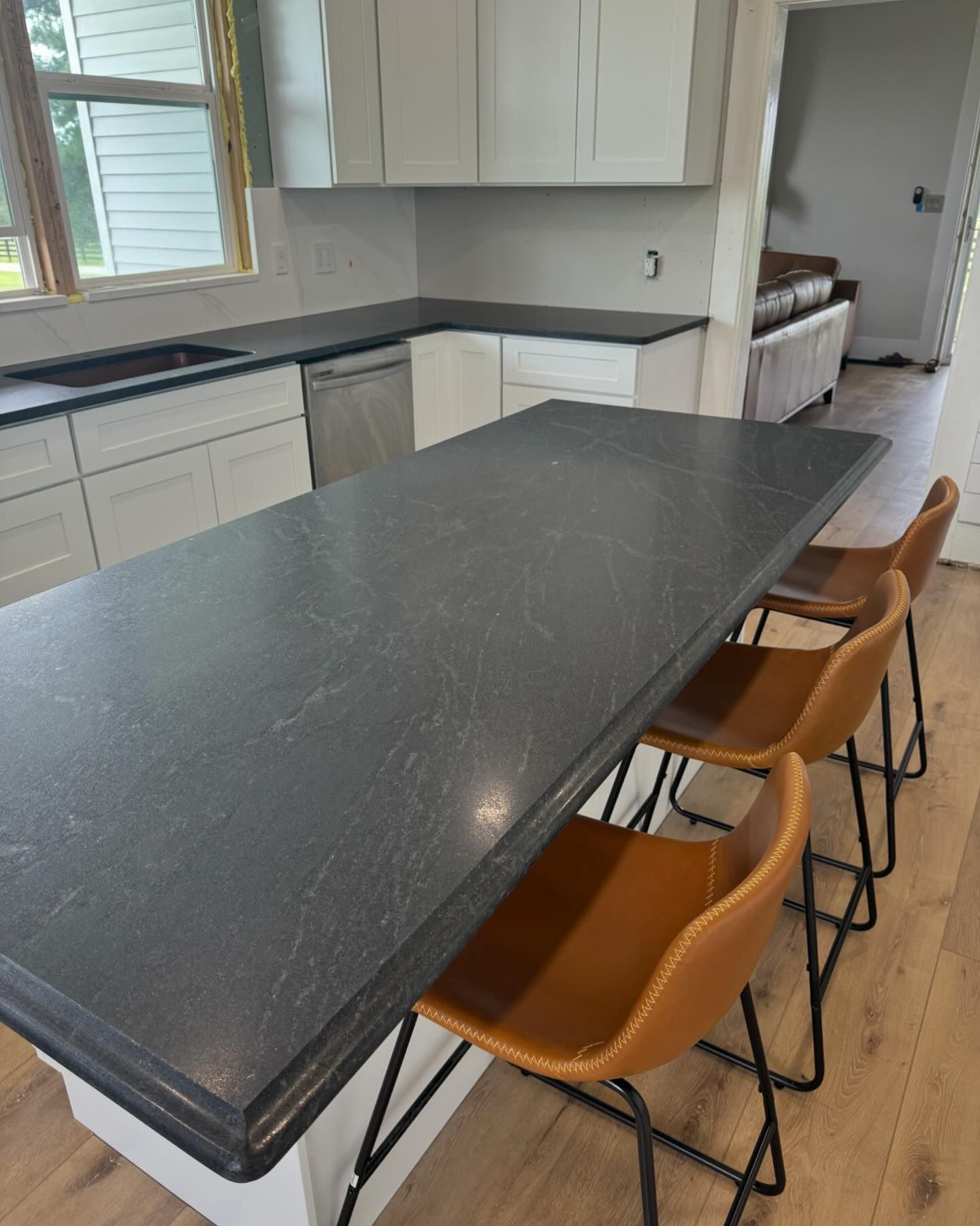 A kitchen with a black counter top and brown chairs