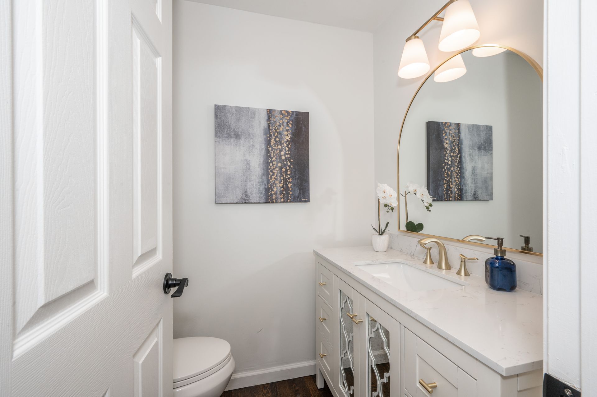 A bathroom with a toilet , sink , mirror and paintings on the wall.