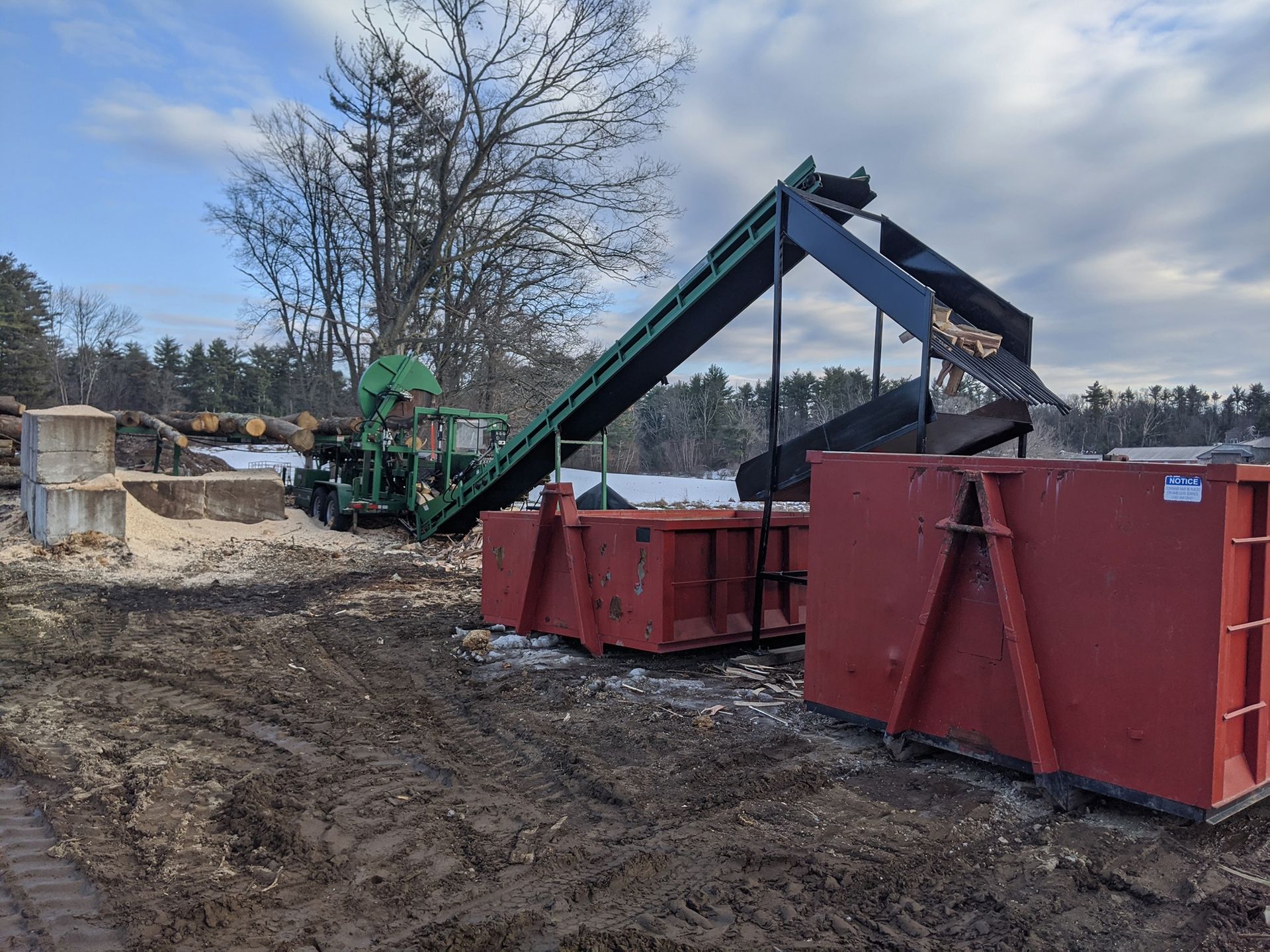 Wood chipper with conveyor belts and two red bins, in a snowy outdoor setting.