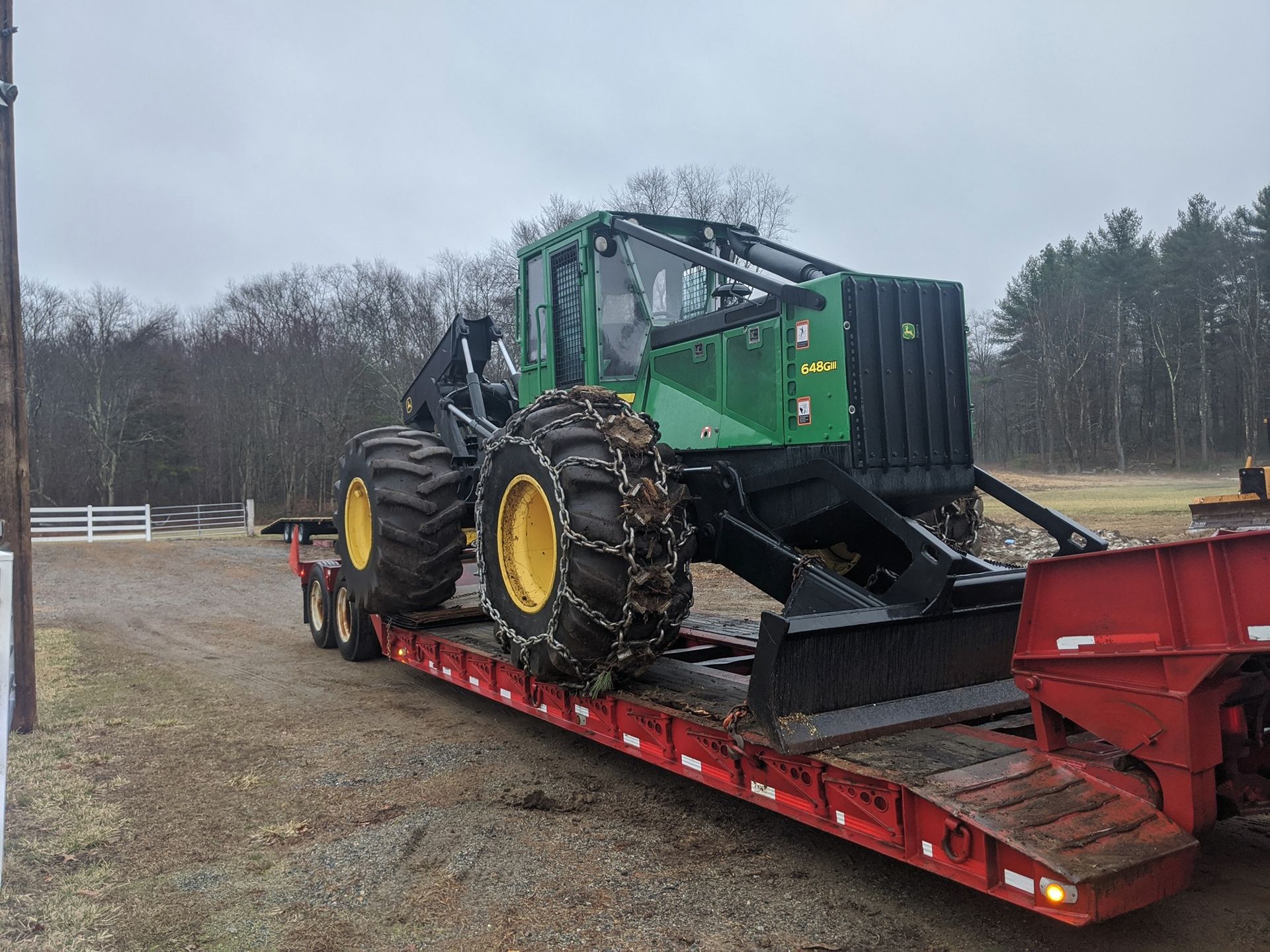 Green and yellow forestry machine on a red trailer, ready for transport outdoors.
