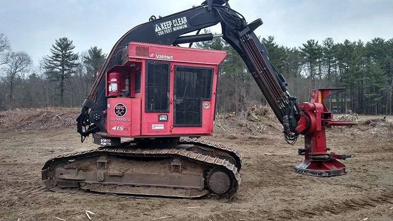 Red forestry harvester on tracks in a clearing.