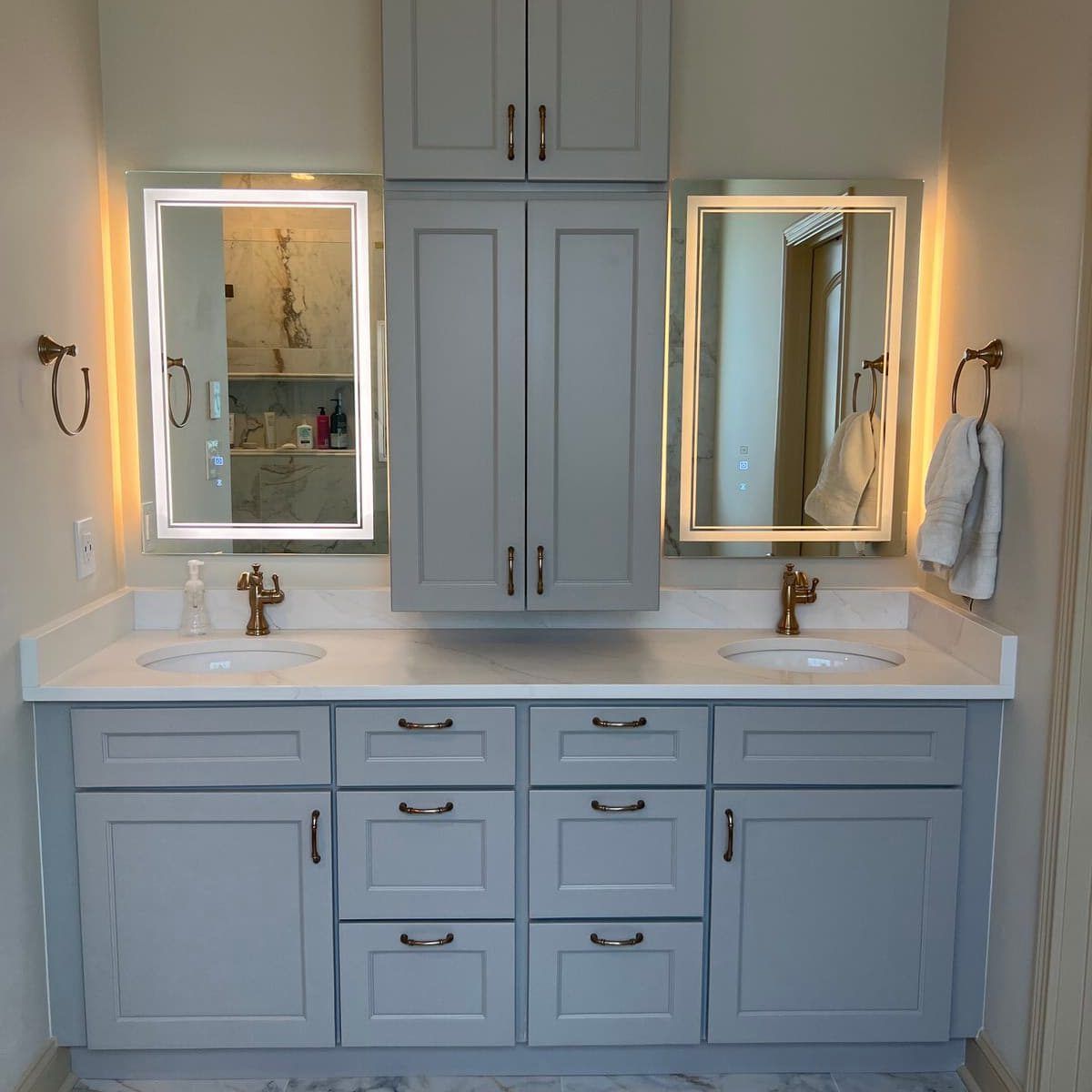 Bathroom vanity with gray cabinets, white countertop, two sinks, and mirrors with LED lighting.