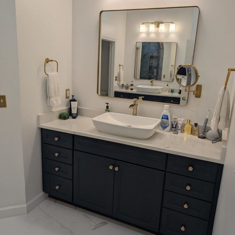 A navy blue bathroom vanity with a white countertop and rectangular vessel sink, gold fixtures, and a large mirror.