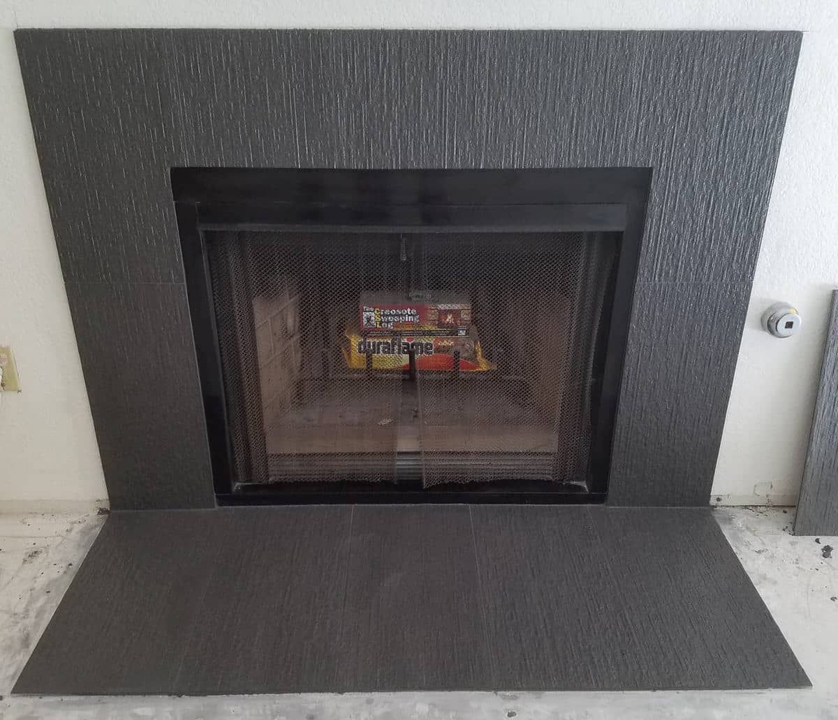 Fireplace with dark textured surround and hearth, fire visible behind a mesh screen.