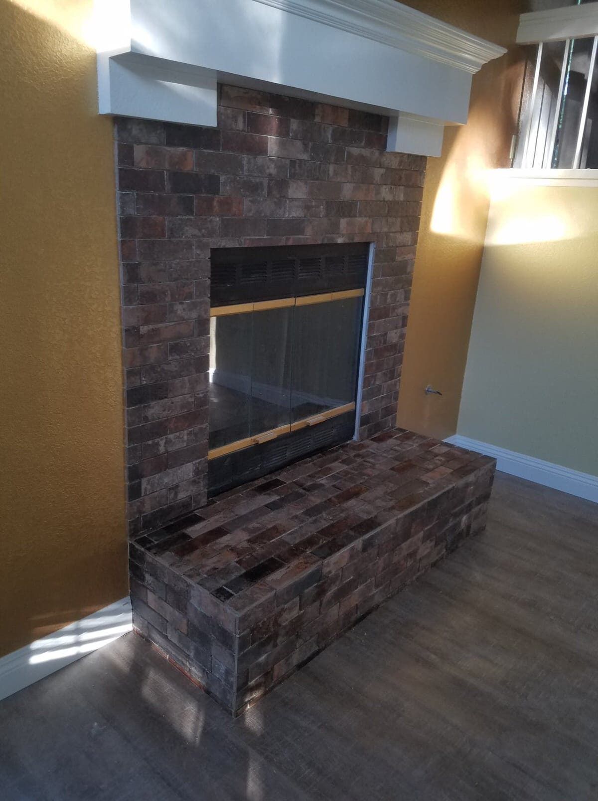 Fireplace with brown brick facade, black glass front, and white mantel in a room with yellow walls.