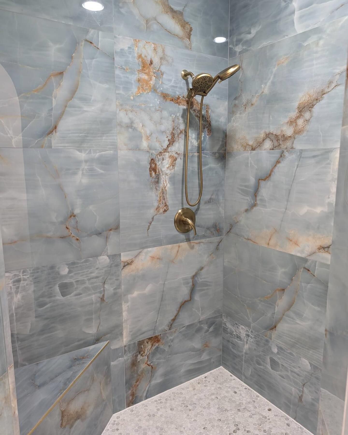 Blue tiled shower with bronze showerhead and corner bench.